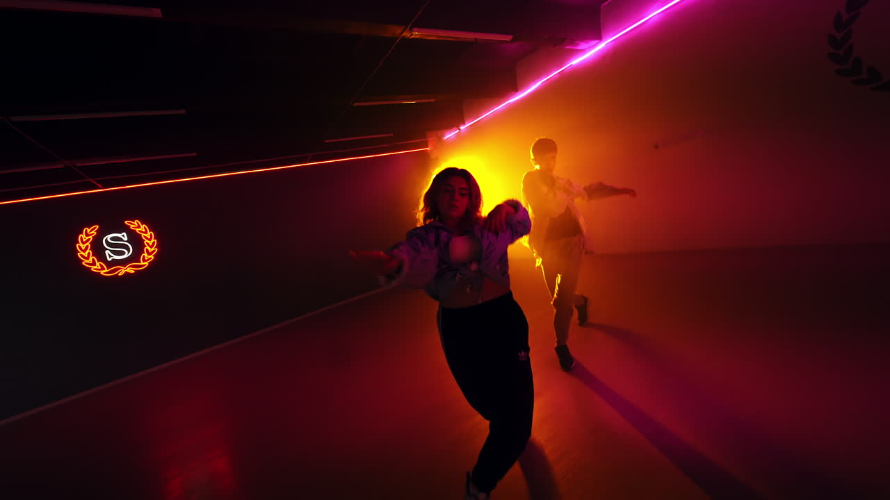 Couple of dancers move energetically. Young people dance hip hop in the studio in yellow light.