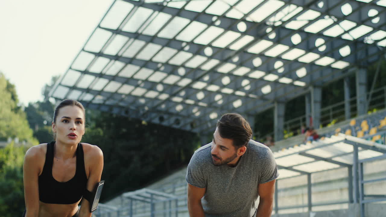 pareja de jóvenes corredores corriendo en el estadio, luego se detienen para descansar y mirar la cámara