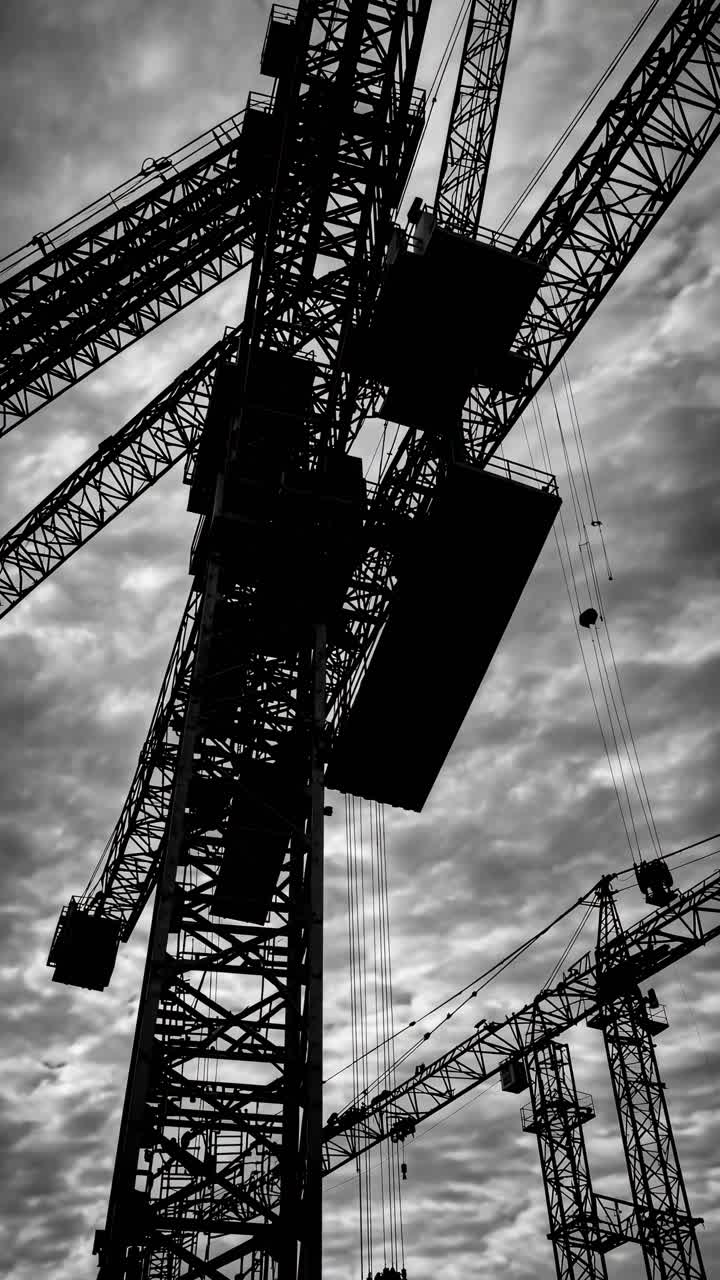 Dramatic low-angle shot of silhouetted cranes against a cloudy sky, perfect for an industrial-themed