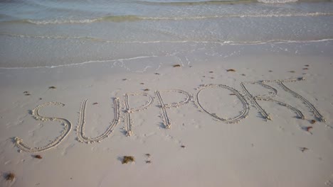 turning shot of support written in the sand on a beach