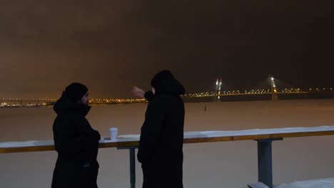 people talking at night on a frozen river with a bridge in the background