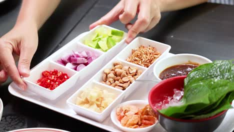 hands assembling traditional thai leaf wrap ingredients on table