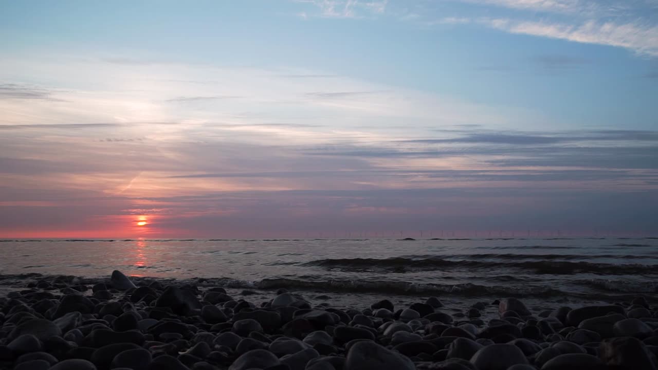 pink sun setting at horizon blue cloudy sky on a rocky beach. time lapse