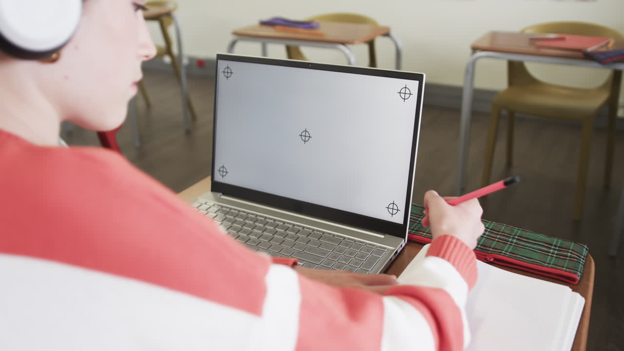 In school, young girl wearing headphones writing notes with laptop, focused on learning, copy space