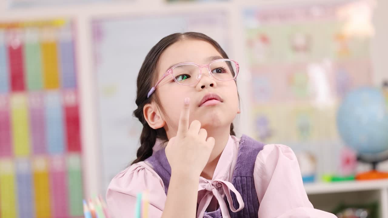 Young girl with glasses ponders thoughtfully at desk in brightly lit primary school classroom