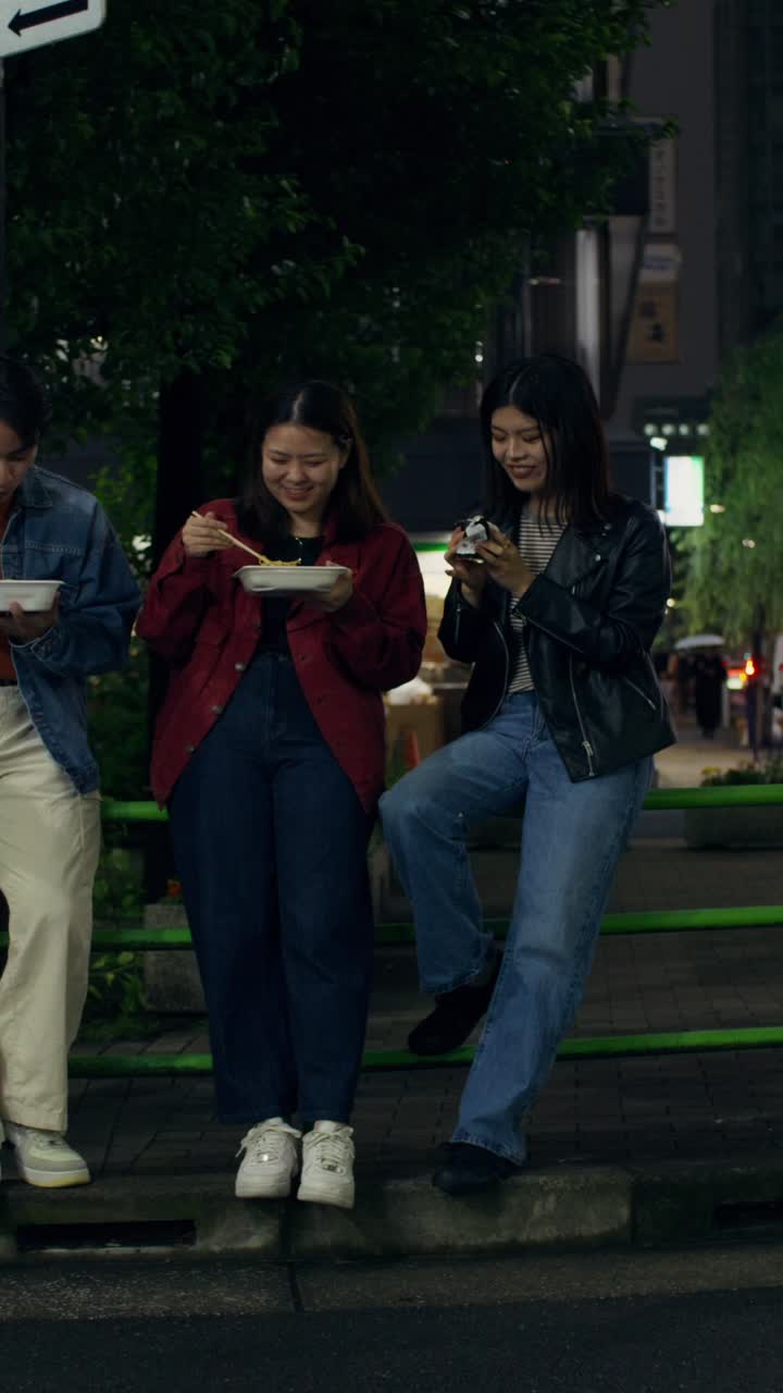 Friends Eating Noodles on a City Street at Night
