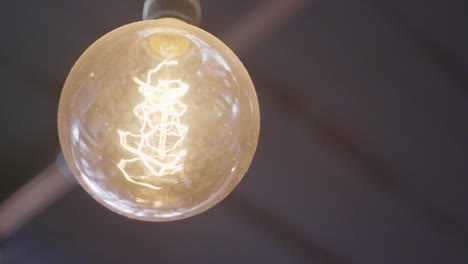 close up of a hanging warm glowing vintage looking light bulb with a twisted filament inside