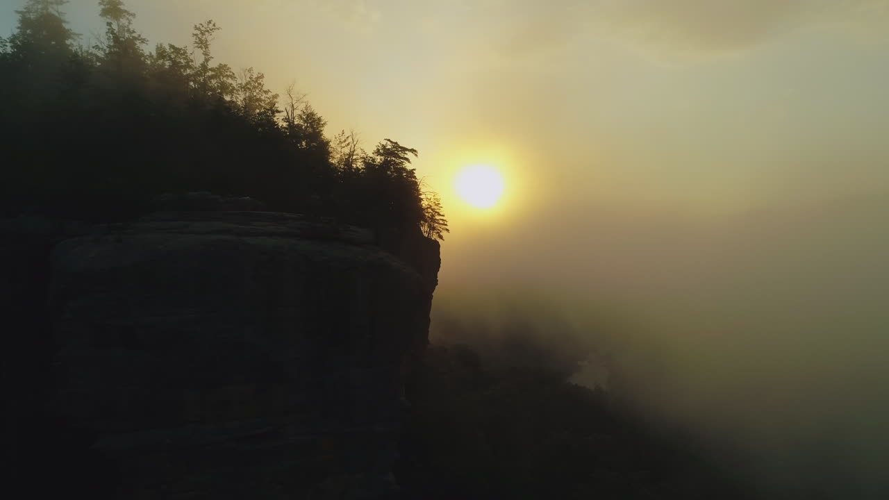 aérea orbitando dos siluetas en el acantilado durante el brumoso amanecer dorado, 4k