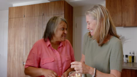 multiracial senior female friends enjoying conversation while preparing food in kitchen, at home