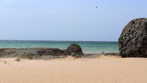 magnífica escena cinematográfica en la orilla del mar verde esmeralda con rocas y arena girando en el aire en una impresionante resolución de 4k