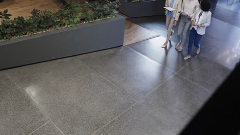 diverse female colleagues in discussion using tablet in office foyer, slow motion