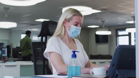 mujer con máscara facial usando computadora en la oficina