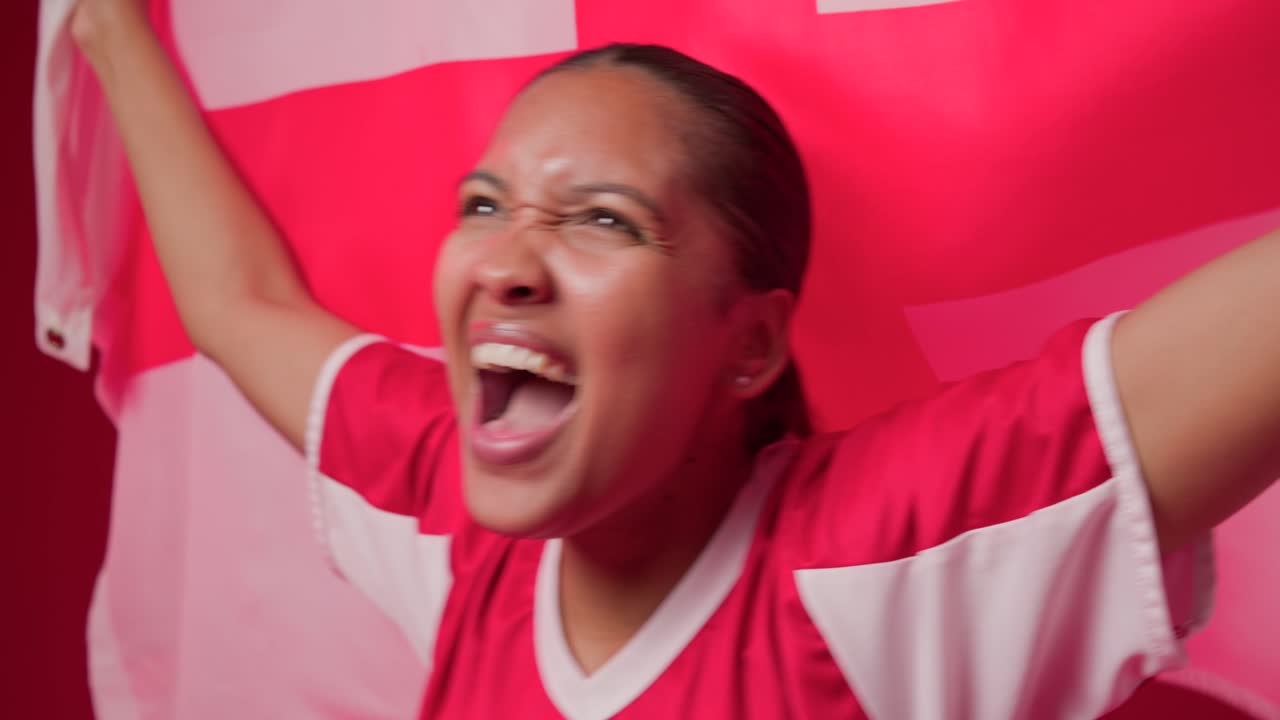 African American female in red jersey cheering for goal, shouting and waving red-white flag on set