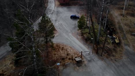 Drone-shot-descending-and-tilting-up,-filming-a-car-parked-on-the-other-side-of-an-old-gate