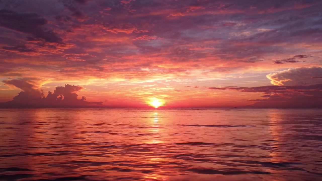 Un tramonto mozzafiato che dipinge il cielo con vivaci sfumature di arancione, rosa e viola, riflesso sulle calme acque dell'oceano, creando un'atmosfera serena e tranquilla.