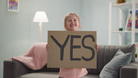 joyful girl holds sheet with word yes standing in room