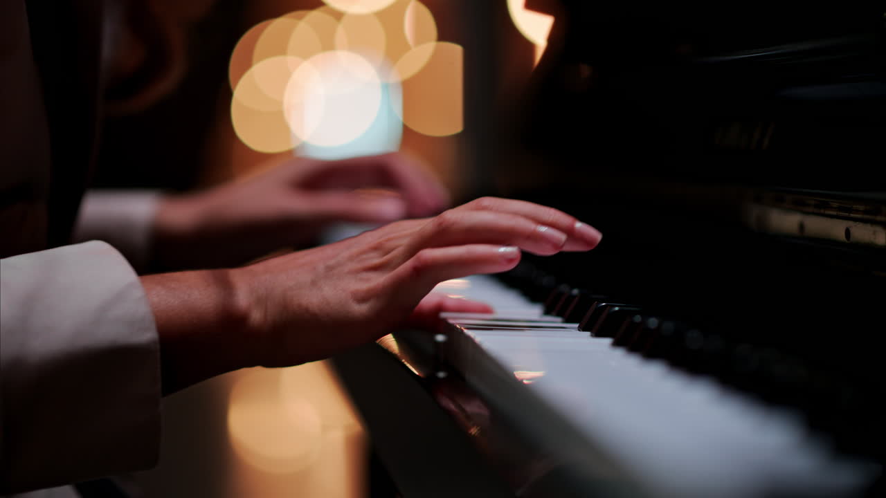 Close up of a woman's hands playing the piano with blurry lights on the background