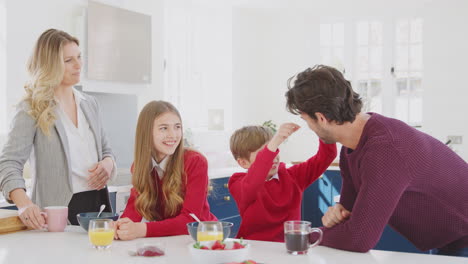 Padres-Ayudando-A-Niños-En-Uniforme-Escolar-A-Prepararse-Mientras-Desayunan-En-El-Mostrador-De-La-Cocina