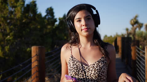 beautiful young hispanic woman listening to music on her headphones and smartphone while smiling and being happy slow motion