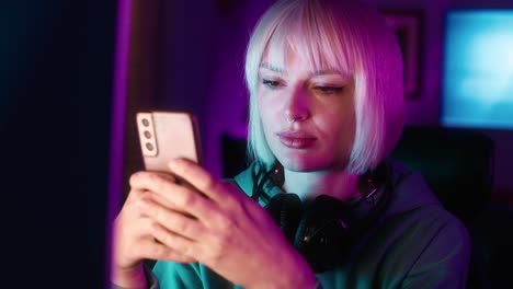 serious young caucasian woman browsing mobile phone while a break during playing game at night on desktop pc