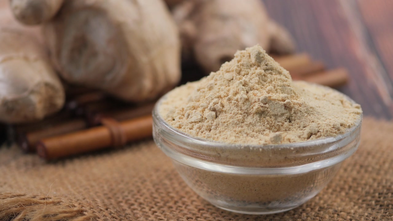 Close-up of Ginger Powder in a Glass Bowl with Ginger Roots and Cinnamon