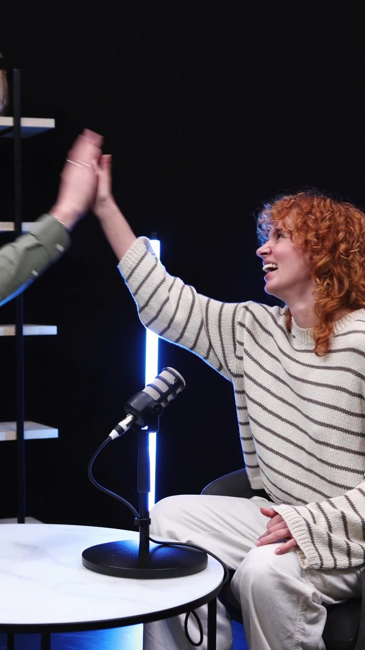 Mujer pelirroja feliz chocando las cinco durante la grabación de un podcast en un estudio