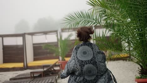 back view of a barefoot woman in a graceful peignoir running by resort beach on a summer day, slowmo