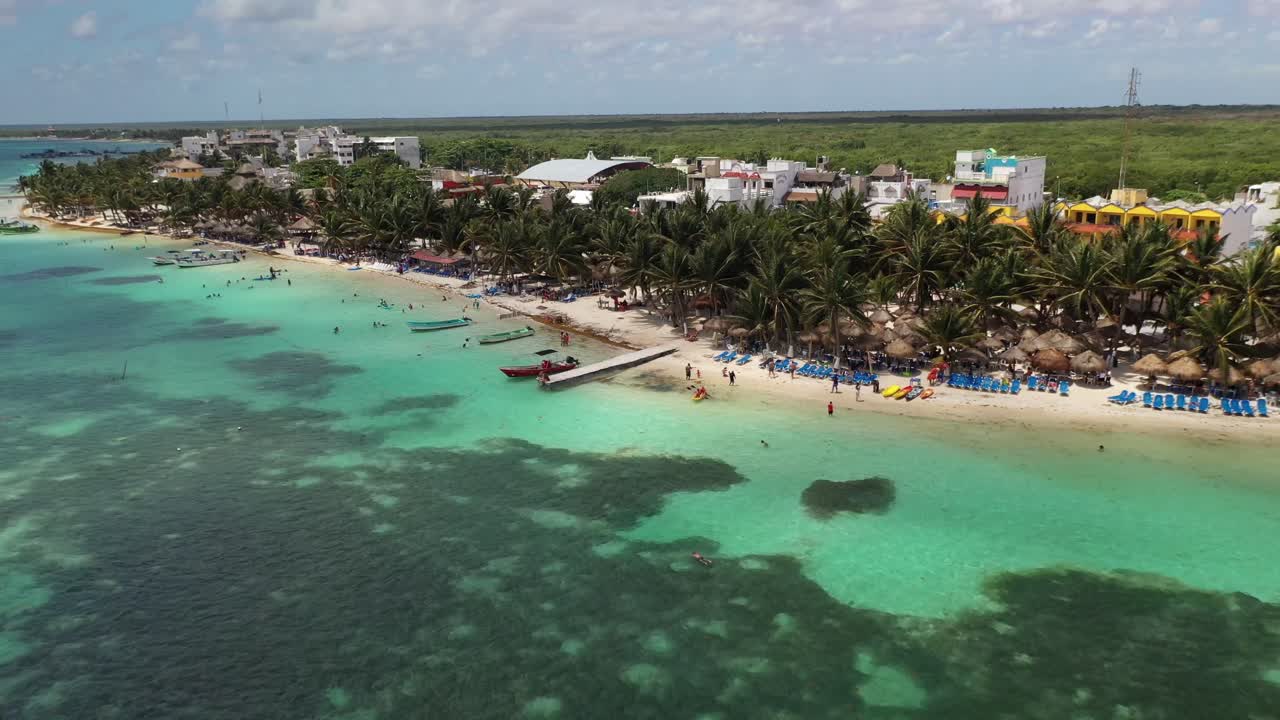 Impresionante vista aérea de Bacalar, México, con aguas cristalinas de laguna turquesa, playa bordeada de palmeras y cabañas con techo de paja. Escena de paraíso tropical con gente disfrutando de la costa caribeña