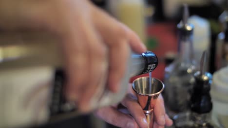 il barista versa l'alcool in un bicchiere di metallo preparando un cocktail, da vicino