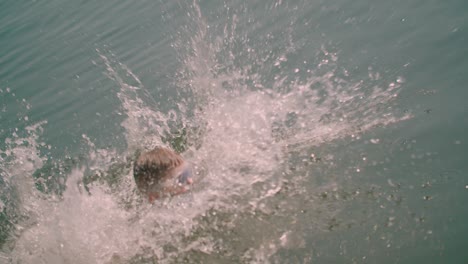 Close-up-view-of-a-Caucasian-kid-runs-jumping-into-the-lake-from-the-wooden-pier