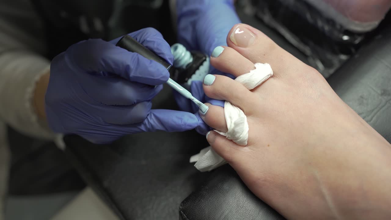 manicurist applying baby blue color nail polish on customer's toenails