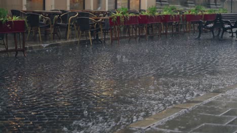 stream of water are flowing through the pavement in rainy weather. Raindrops is falling on the road against the background of the summer terrace of the restaurant
