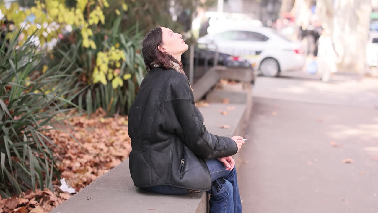 Woman sitting on a wall smoking a cigarette outdoors