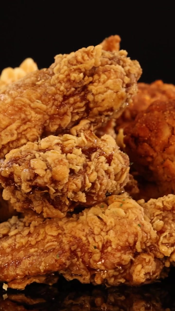 Uno scatto ravvicinato verticale di pollo fritto dorato assortito in rotazione su sfondo nero.