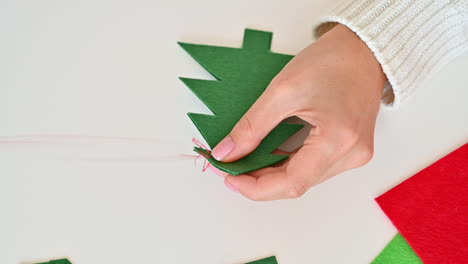 woman hands sew two christmas trees cut out of green fabric using red thread