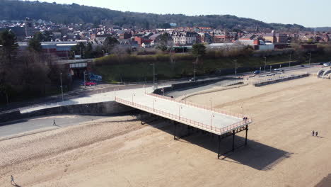 an aerial view of colwyn bay seafront and small fishing jetty on a sunny day, flying left to right around the jetty, denbighshire, north wales, uk