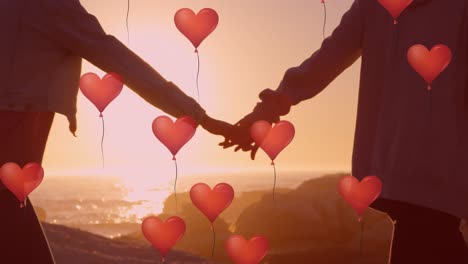 Multiple-heart-balloons-floating-against-couple-holding-hands-and-walking