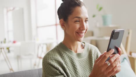 Video-of-happy-biracial-female-designer-using-smartphone-in-studio