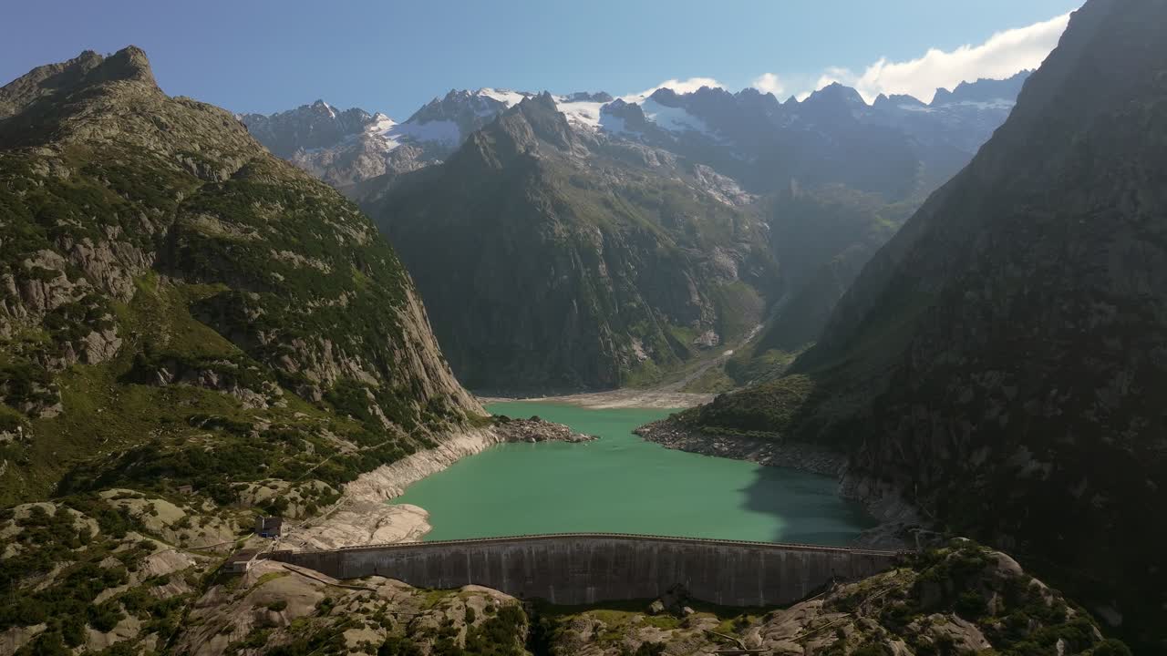 Aerial shot of Gelmersee Lake in the Swiss Alps, showing the turquoise water of the mountain reservoir framed by steep granite cliffs and alpine peaks under a clear summer sky