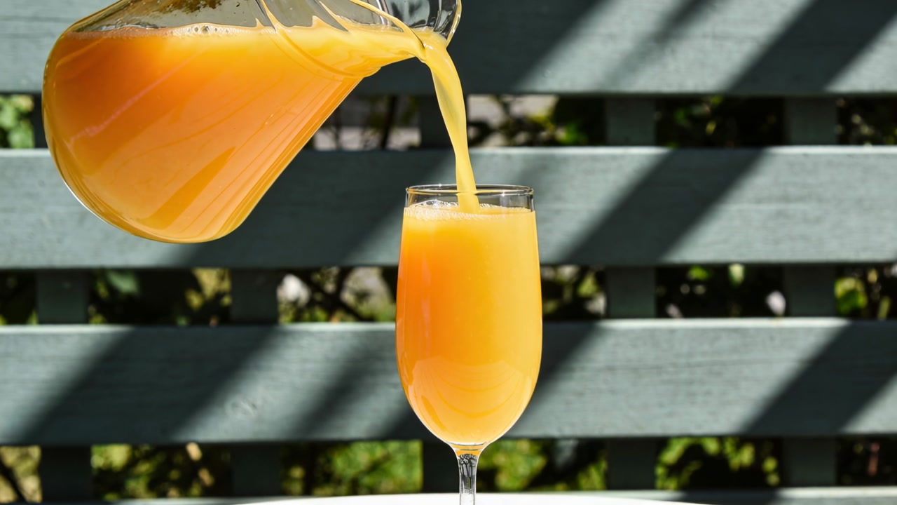 Vertical video: Pitcher tilting pouring OJ into tall glass avoiding overflow, slats shadows for ads