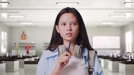 close up of asian teen girl student with a backpack taking note on notebook and thinking then raising her index finger while standing in science laboratory