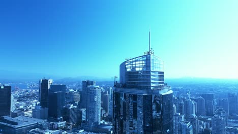 Moderno-Edificio-Ovalado-De-Vidrio-Con-Vista-Al-Centro-De-Vancouver-Día-Soleado-De-Verano-Con-Un-Edificio-De-Baja-Altura-Que-Rodea-El-Enorme-Edificio-Del-Hotel-Con-El-Horizonte-De-Coquitlam-En-El-Horizonte