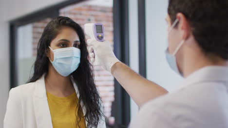 man wearing face mask checking temperature of woman at office