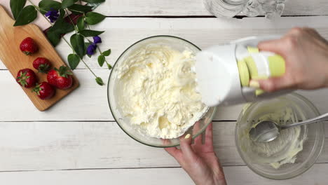 top down shot of mixing whipped heavy cream with melted white chocolate in glass bowl using hand mixer