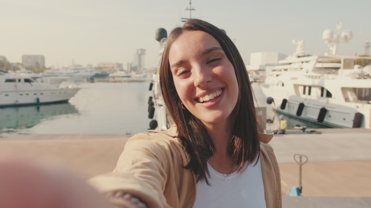 Happy Young Woman Waving and Smiling During a Selfie Video Call at Marina