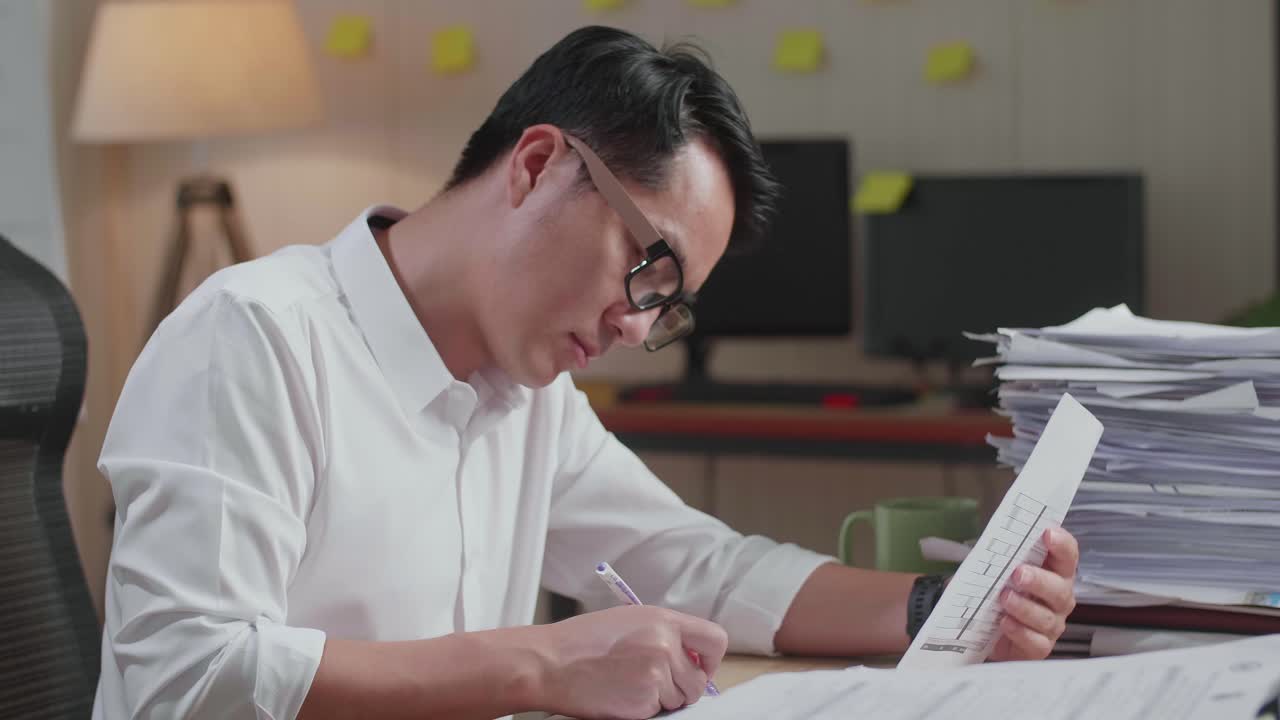 Close Up Of Asian Man Writing Something On Paper While Working With Documents At The Office