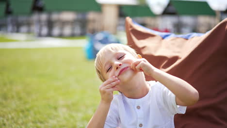 five-year-old boy making faces sitting outdoors. little kid having fun resting in bean bag chair in the bright sun. close up.