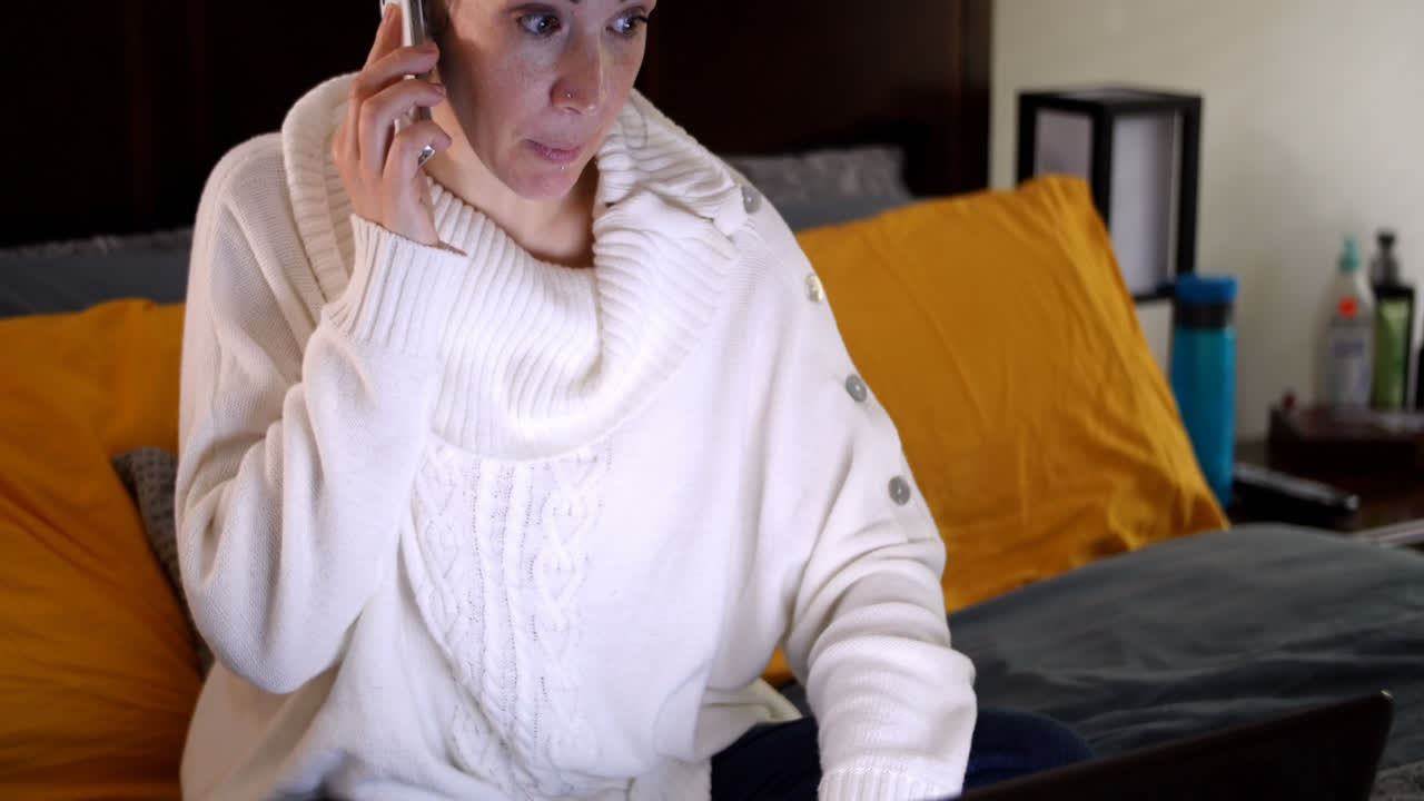 женщина разговаривает по мобильному телефону и использует ноутбук на кровати