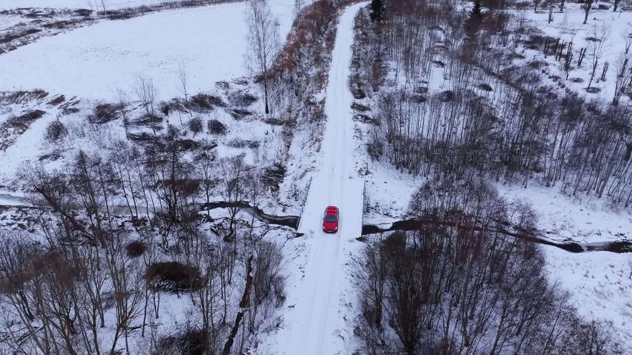 Drone flies backward following red car driving snowy bridge cinematic travel