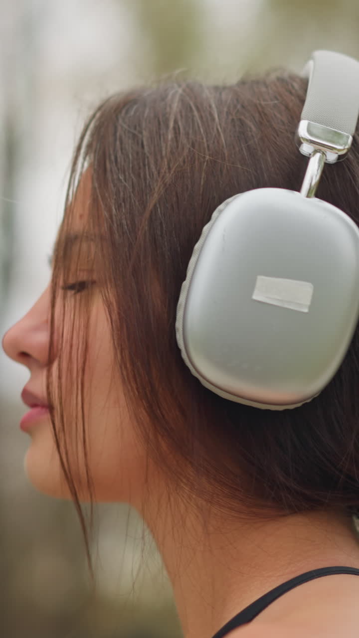 Side view of a young lady wearing headphones, focused and adjusting the volume on her headphones, with blurred natural background, perfect for videos about music, tech, or concentration